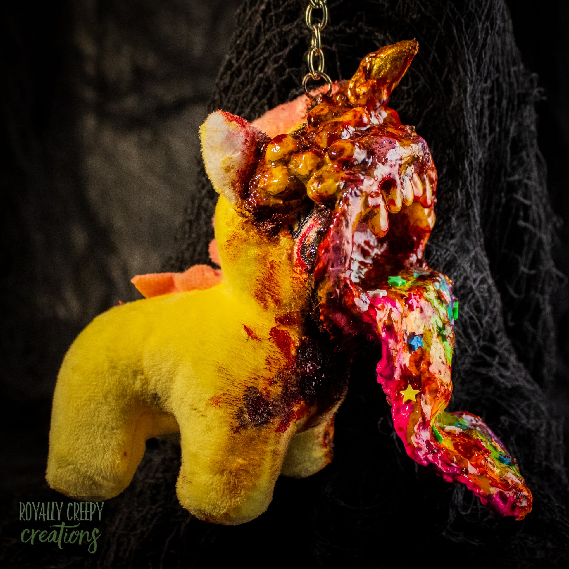 A creepy, horror-themed keychain featuring a plush unicorn vomiting up a rainbow.