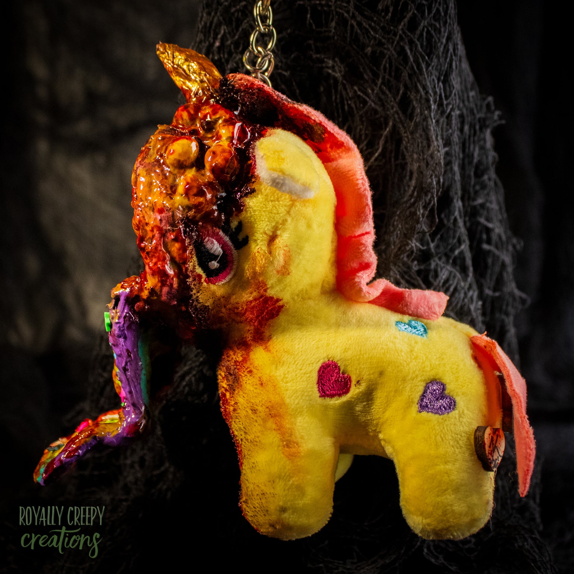 A creepy, horror-themed keychain featuring a plush unicorn vomiting up a rainbow.