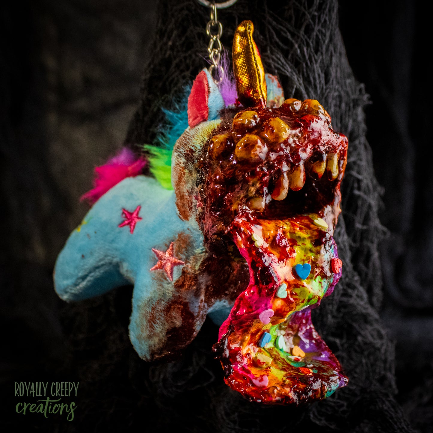A creepy, horror-themed keychain featuring a plush unicorn vomiting up a rainbow.