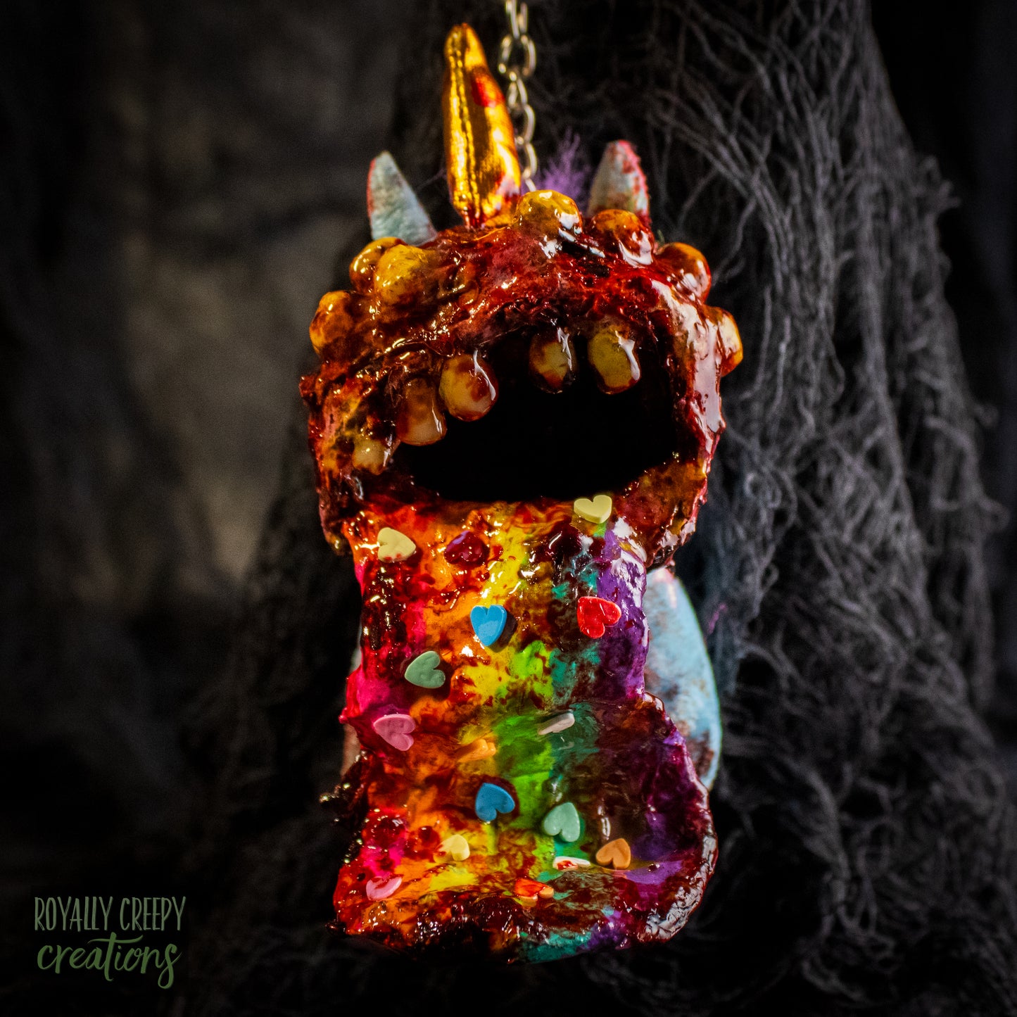 A creepy, horror-themed keychain featuring a plush unicorn vomiting up a rainbow.