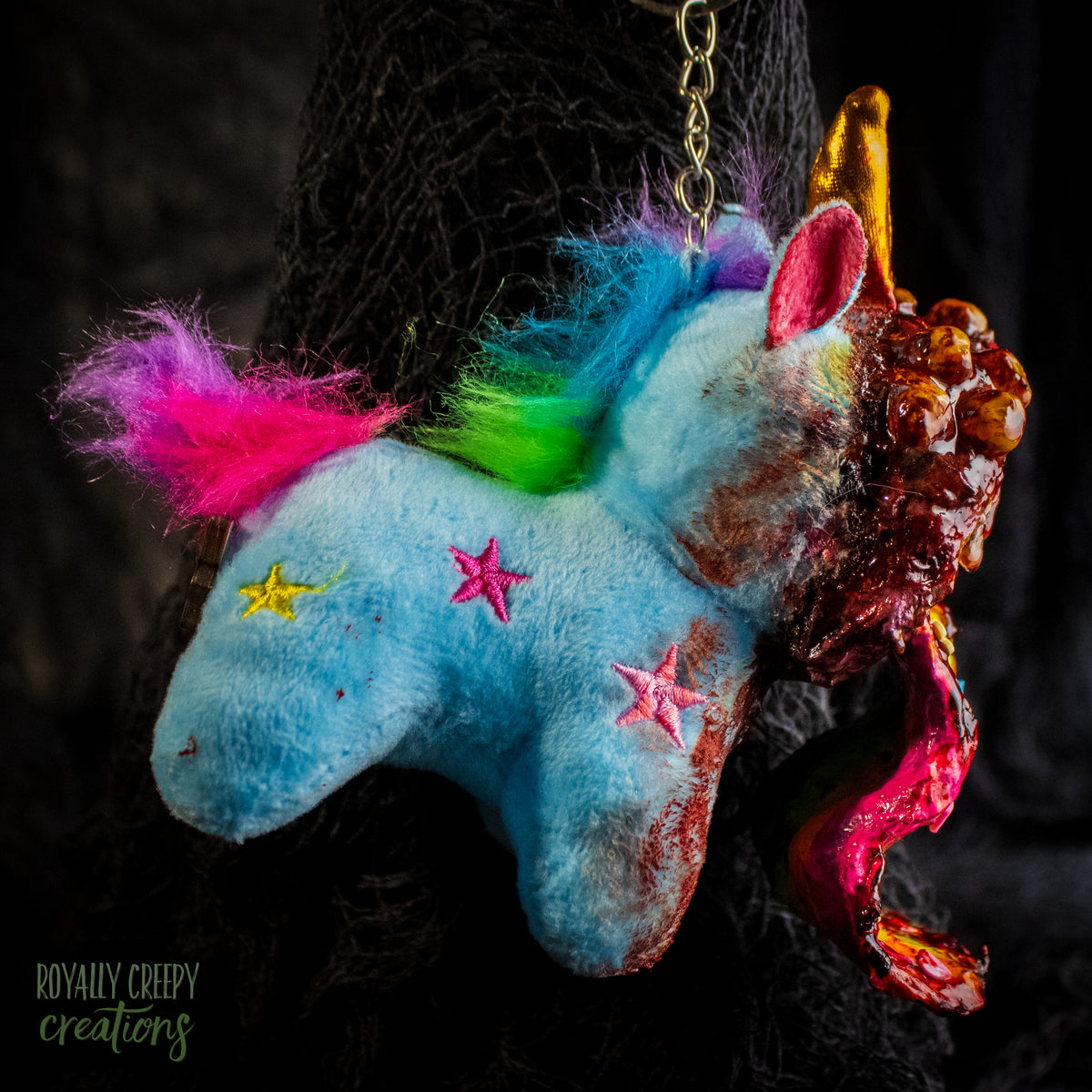 A creepy, horror-themed keychain featuring a plush unicorn vomiting up a rainbow.