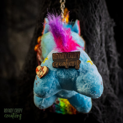Back view of a blue plush unicorn  with a wooden 'Royally Creepy Creations' brand tag.