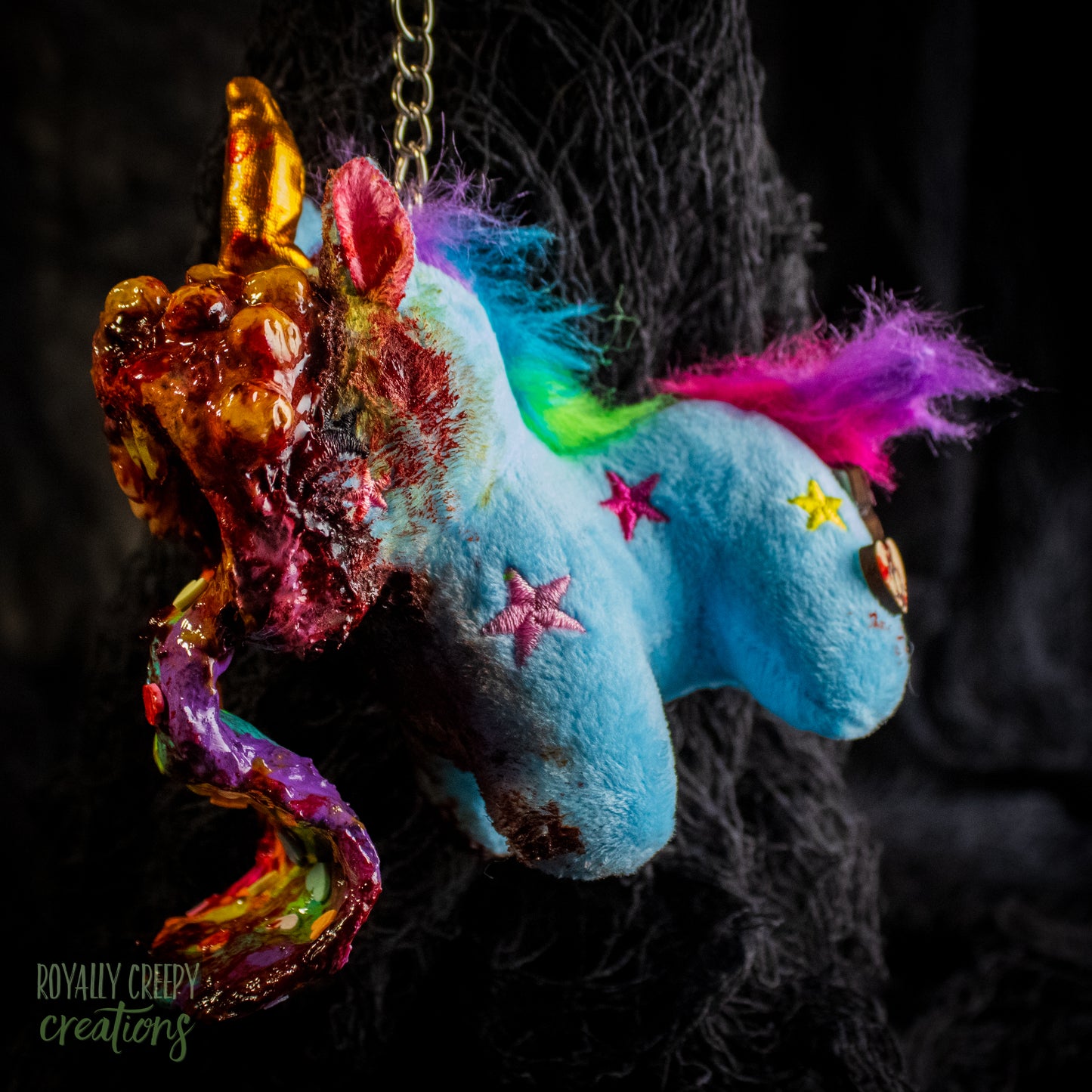 A creepy, horror-themed keychain featuring a plush unicorn vomiting up a rainbow.