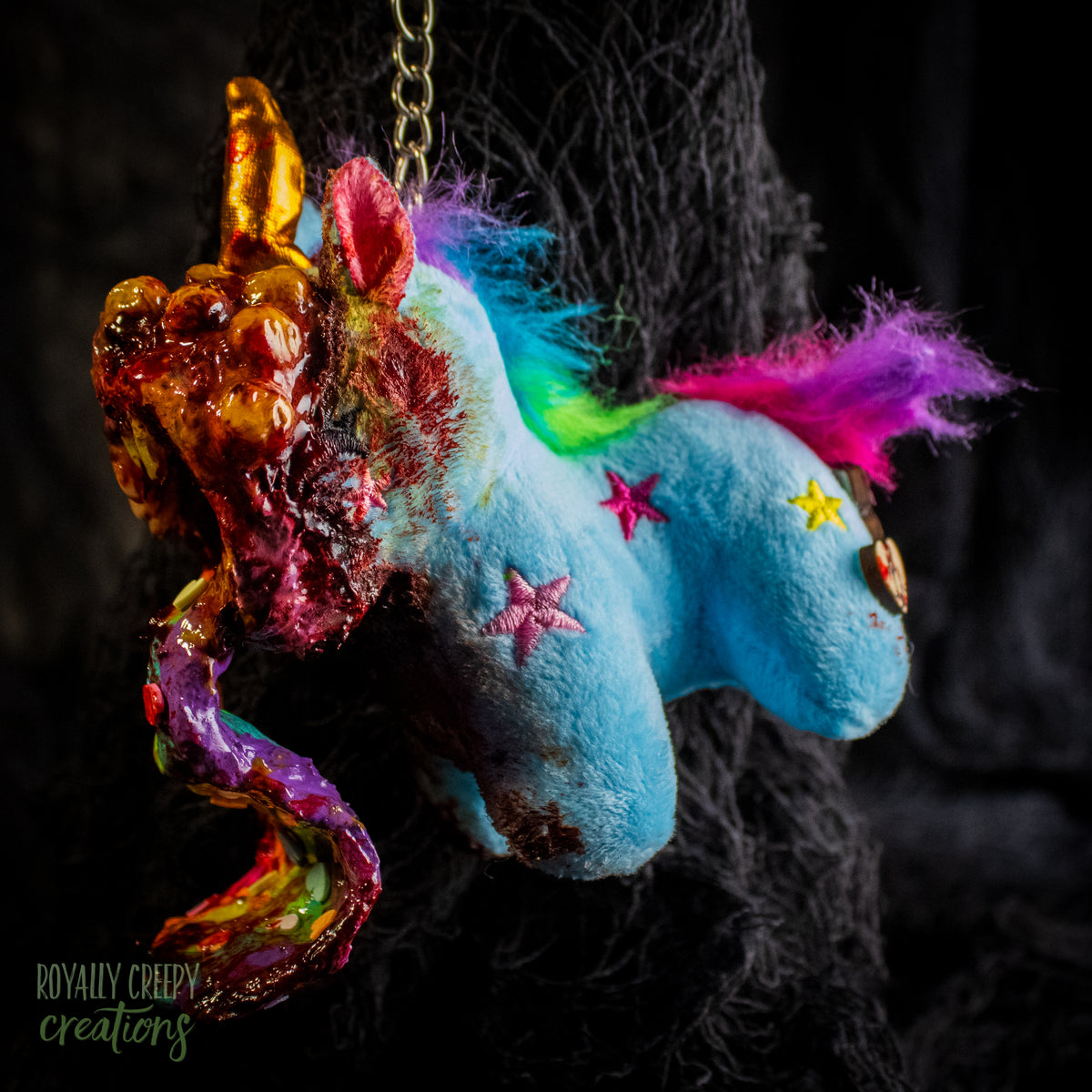 A creepy, horror-themed keychain featuring a plush unicorn vomiting up a rainbow.