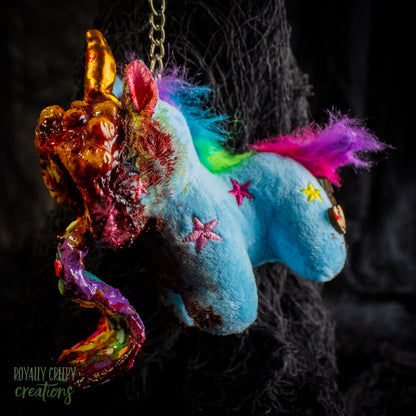 A creepy, horror-themed keychain featuring a plush unicorn vomiting up a rainbow.