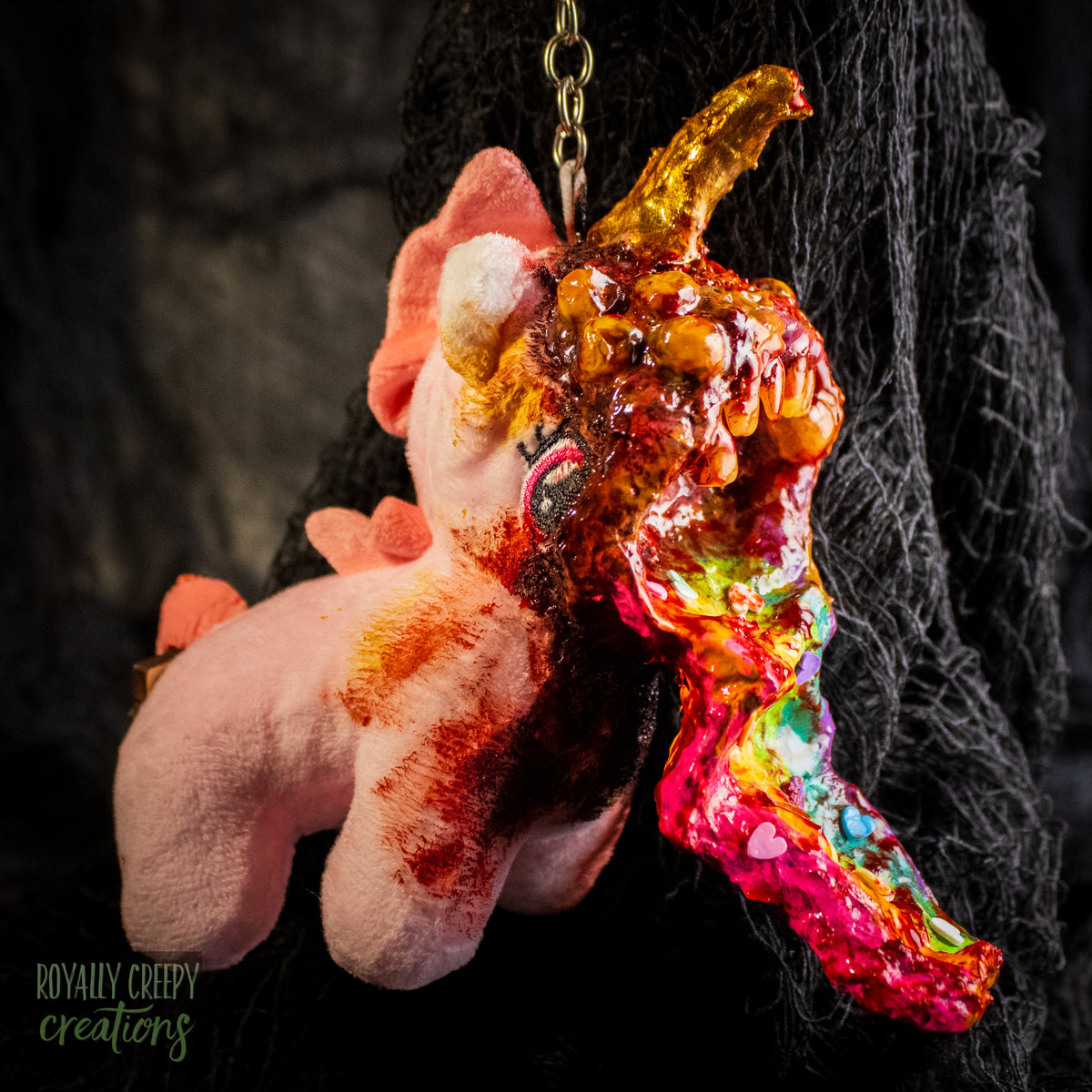 A creepy, horror-themed keychain featuring a plush unicorn vomiting up a rainbow.