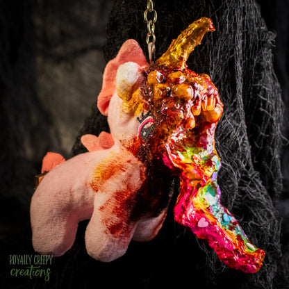 A creepy, horror-themed keychain featuring a plush unicorn vomiting up a rainbow.