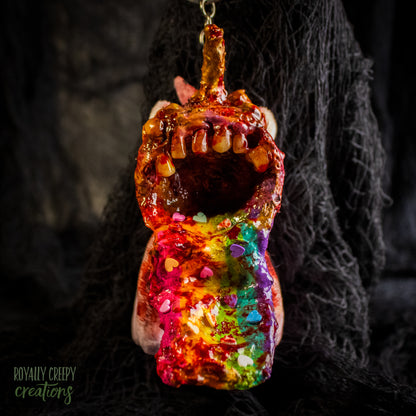 A creepy, horror-themed keychain featuring a plush unicorn vomiting up a rainbow.