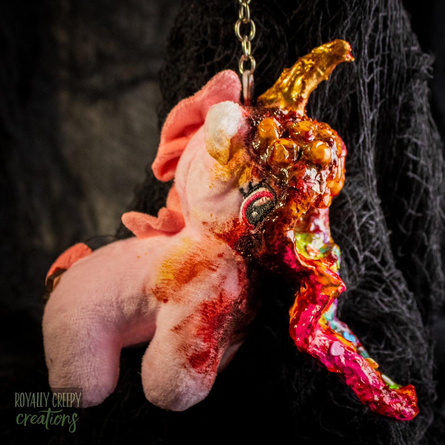A creepy, horror-themed keychain featuring a plush unicorn vomiting up a rainbow.