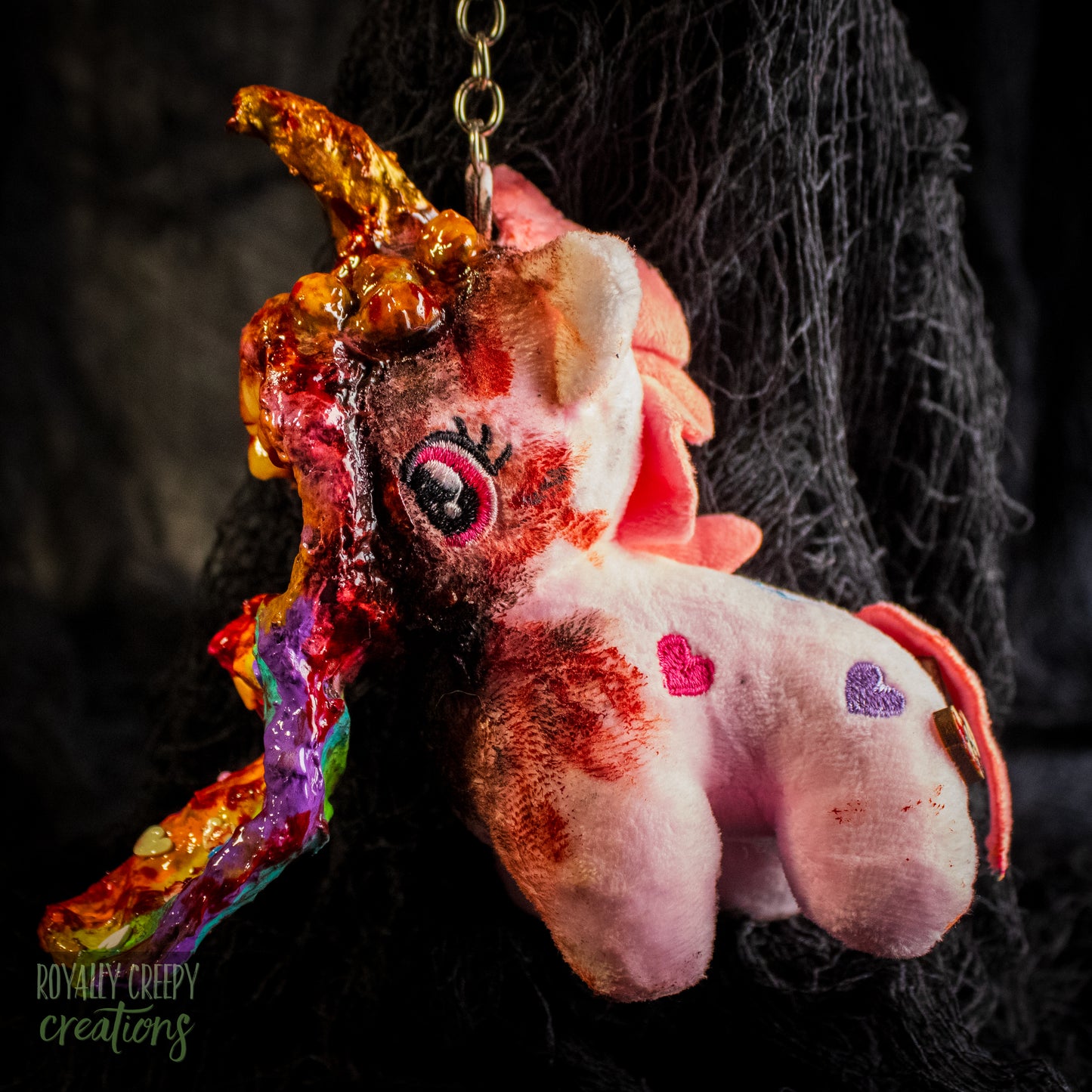 A creepy, horror-themed keychain featuring a plush unicorn vomiting up a rainbow.