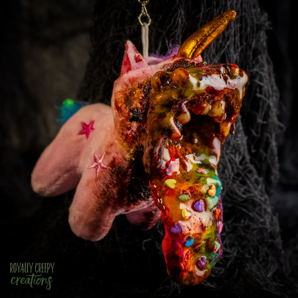 A creepy, horror-themed keychain featuring a plush unicorn vomiting up a rainbow.