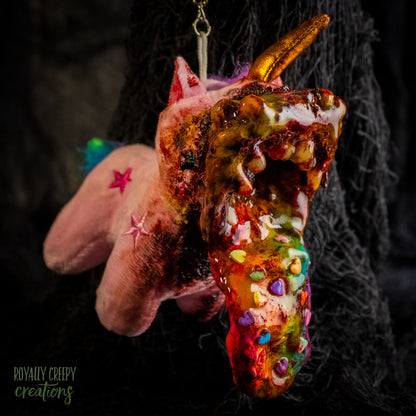 A creepy, horror-themed keychain featuring a plush unicorn vomiting up a rainbow.