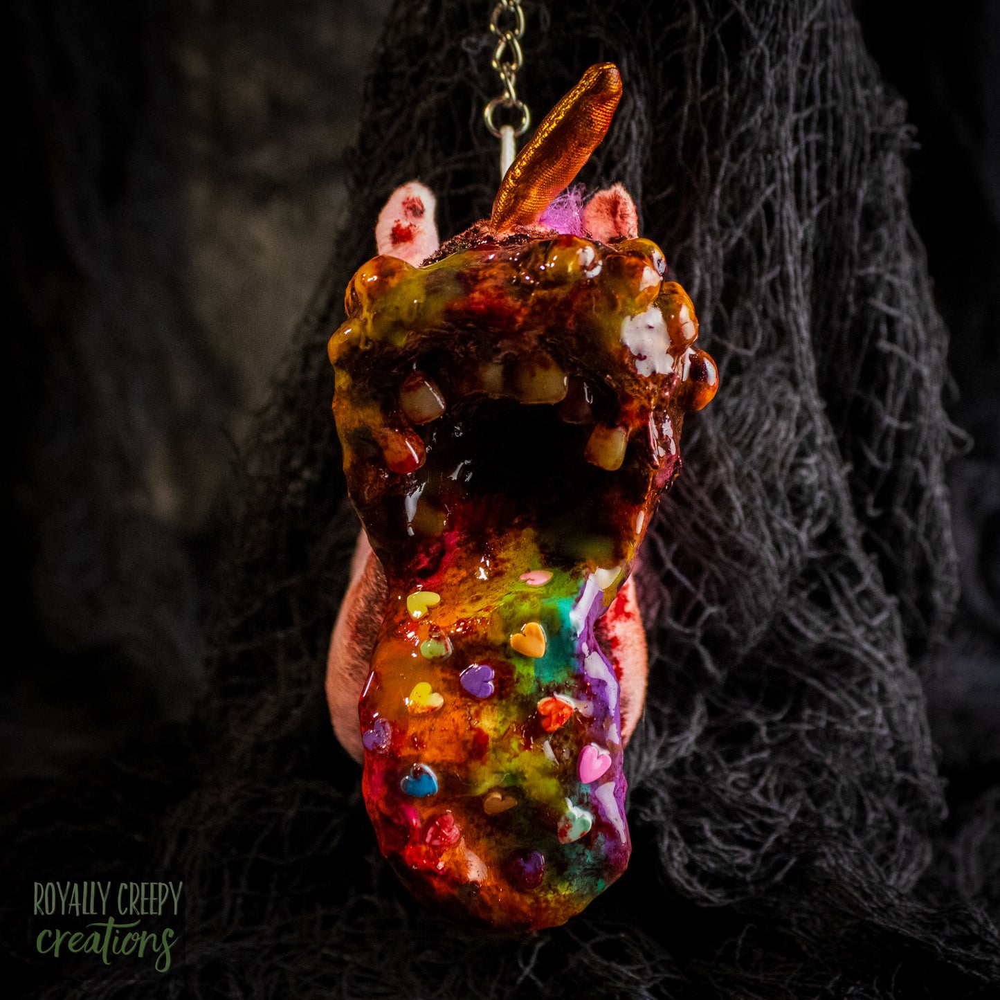 A creepy, horror-themed keychain featuring a plush unicorn vomiting up a rainbow.
