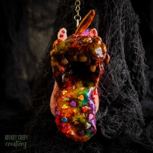 A creepy, horror-themed keychain featuring a plush unicorn vomiting up a rainbow.