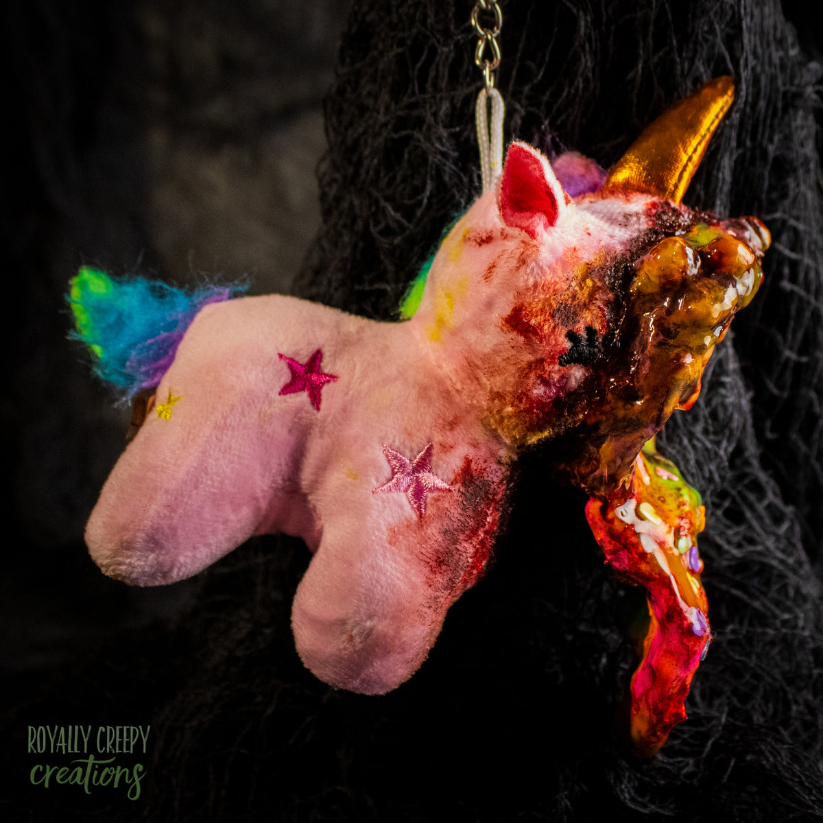 A creepy, horror-themed keychain featuring a plush unicorn vomiting up a rainbow.