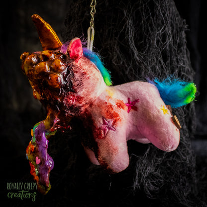 A creepy, horror-themed keychain featuring a plush unicorn vomiting up a rainbow.