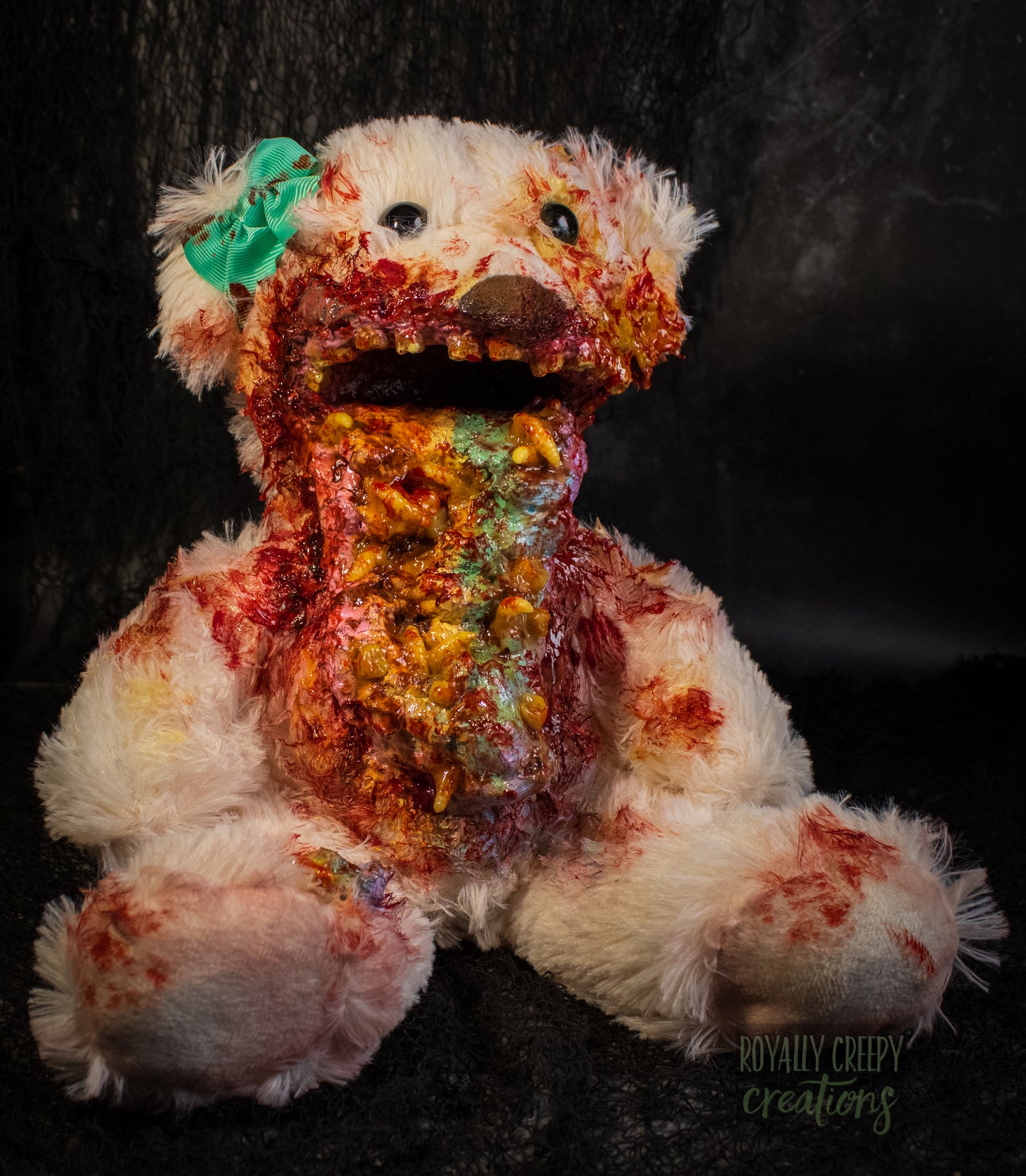 A horror-themed plush teddy bear with a pastel colored vomit & maggots spewing from it's mouth 