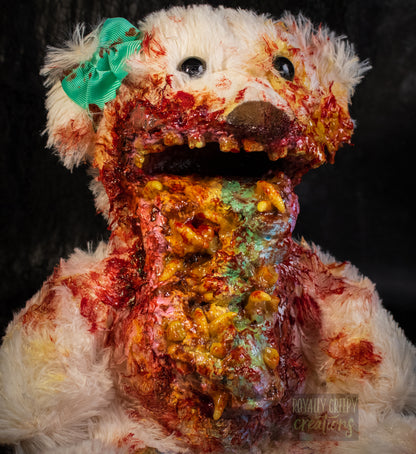 A close up of a horror-themed plush teddy bear with a pastel colored vomit & maggots spewing from it's mouth 