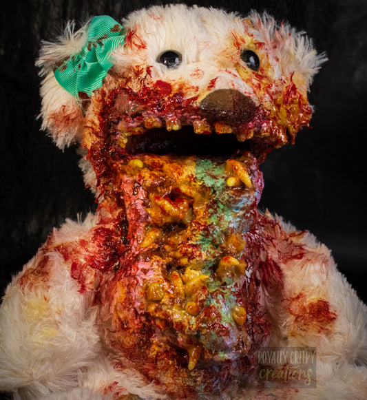 A close up of a horror-themed plush teddy bear with a pastel colored vomit & maggots spewing from it's mouth 