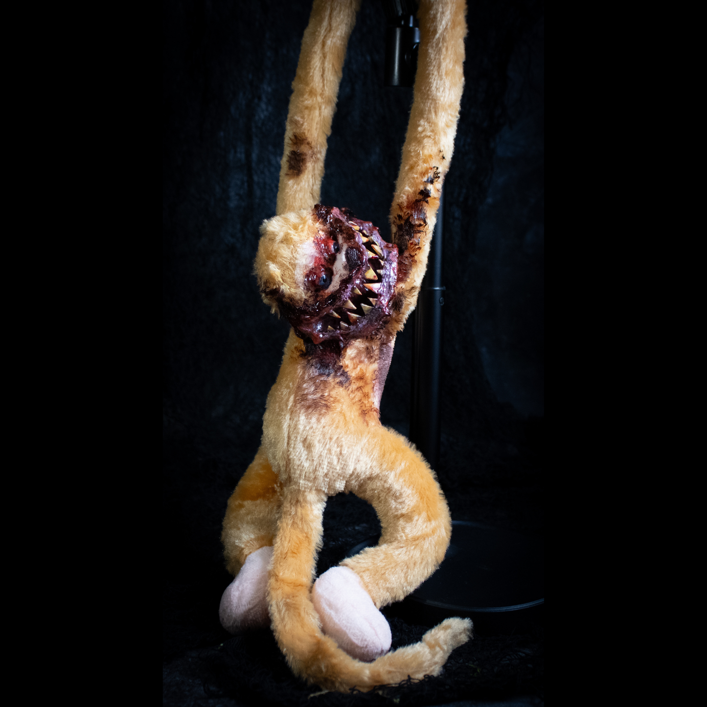 A horror prop of a monkey hanging by its arms against a black background.