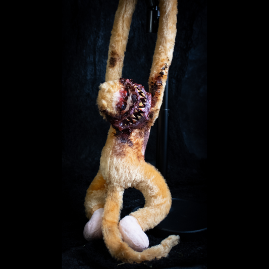 A horror prop of a monkey hanging by its arms against a black background.