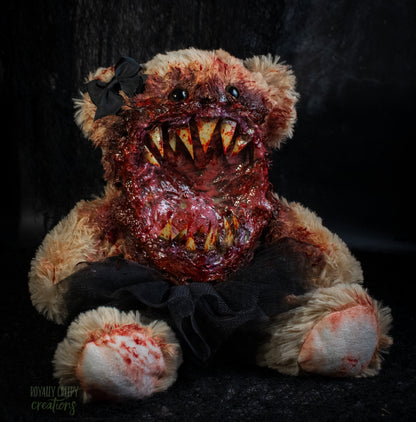 A horror-themed plush teddy bear with a bloody, grotesque mouth showing sharp teeth, a black tutu, and a black bow on its head, set against a dark background.